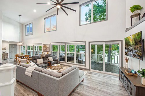 Bright, modern living room with large windows, a cozy sofa, and a view of a deck overlooking a lake.