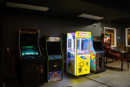 A row of arcade machines, including a claw machine, in a dimly lit game room.