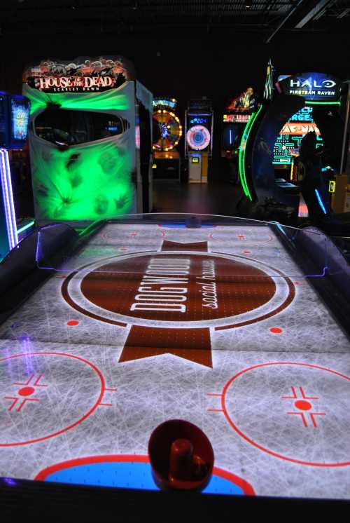 A brightly lit arcade with an air hockey table in the foreground and various games in the background.