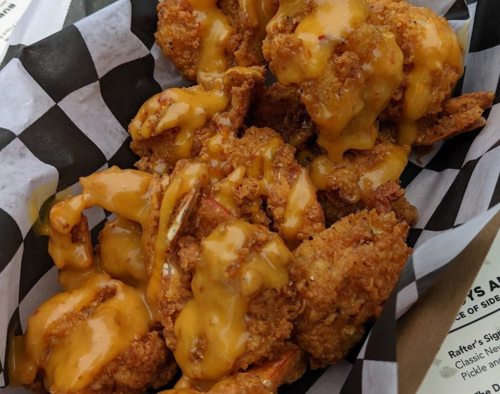 A basket of crispy fried shrimp drizzled with a creamy cheese sauce, served on a checkered paper liner.