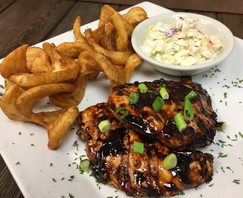 Grilled chicken with a glossy glaze, served with curly fries and coleslaw on a white plate.