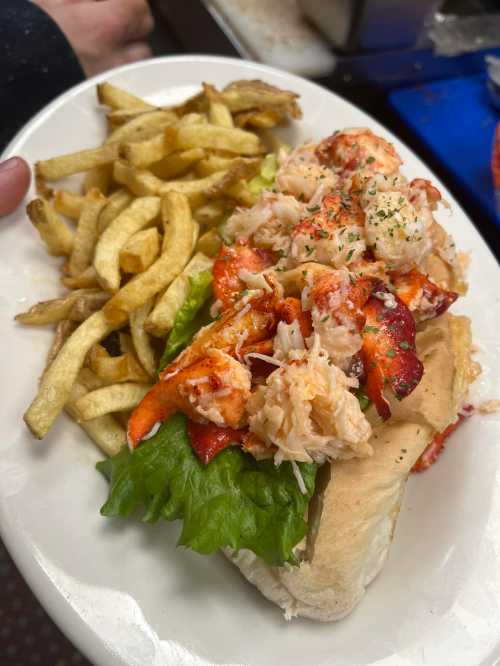 A plate with a lobster roll topped with lobster meat and lettuce, served alongside crispy French fries.