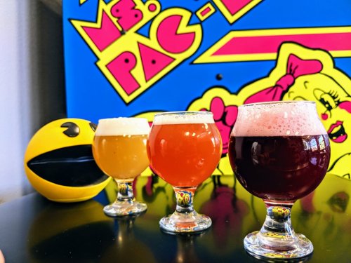 Three colorful beer glasses sit on a table, with a Ms. Pac-Man arcade game in the background.
