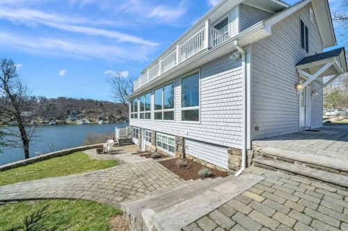 A modern lakeside house with large windows, a stone pathway, and a view of the water under a clear blue sky.
