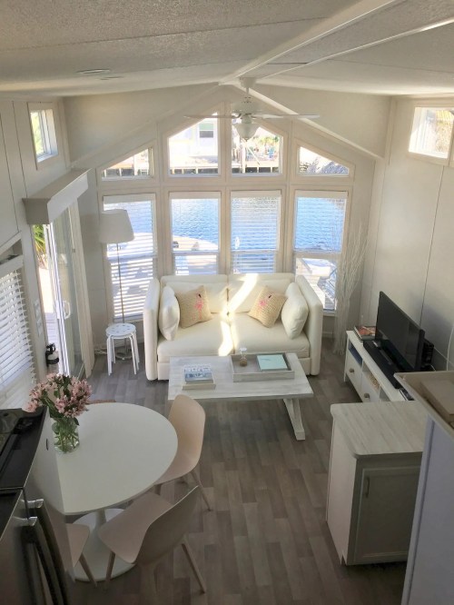 Bright, airy living space with a white sofa, dining table, and large windows overlooking a waterfront view.