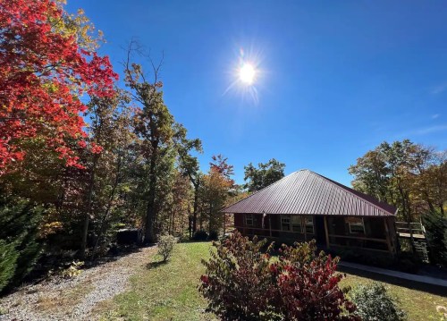 A sunny day with a clear blue sky over a cabin surrounded by colorful autumn foliage.