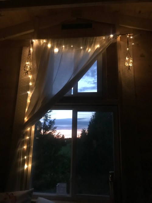 Cozy interior with fairy lights draped by a window, showcasing a sunset and greenery outside.