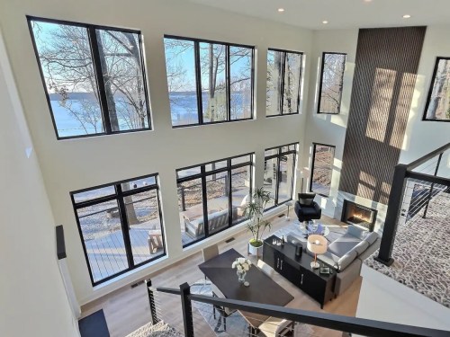 Modern living room with large windows overlooking a lake, featuring a cozy seating area and stylish decor.