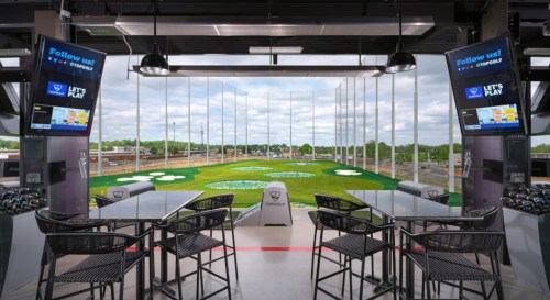 View from a Topgolf bay featuring golf targets, seating, and large screens displaying information.