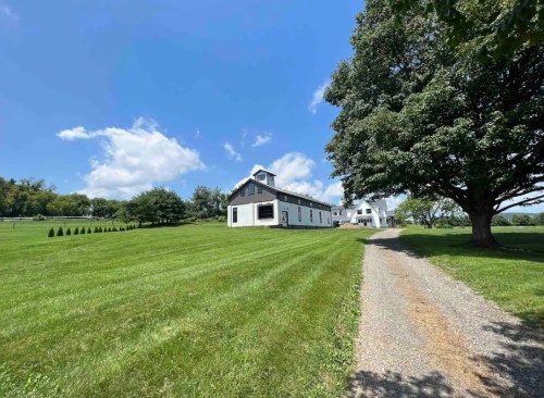A scenic view of a grassy landscape with a white barn and trees under a blue sky with fluffy clouds.