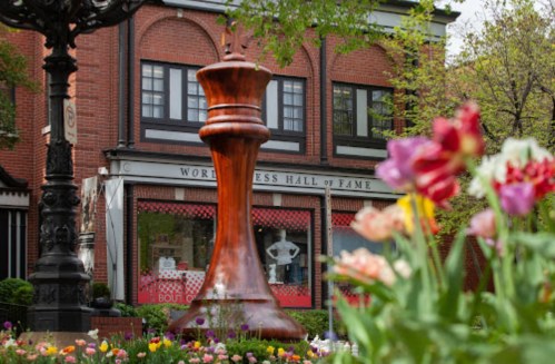 A large wooden chess piece stands in front of the World Chess Hall of Fame, surrounded by colorful flowers.