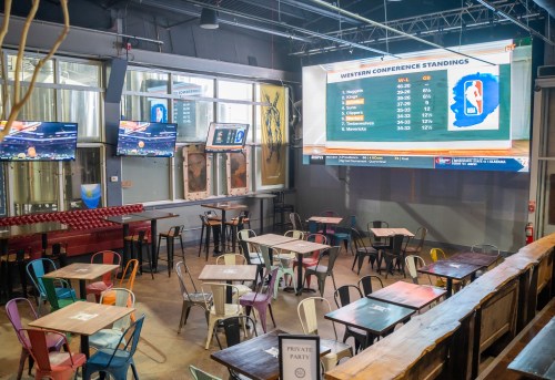 Interior of a sports bar with tables, screens displaying NBA standings, and a casual atmosphere.