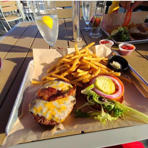 A plate with a cheeseburger topped with bacon, lettuce, tomato, pickles, and a side of crispy fries and dipping sauces.