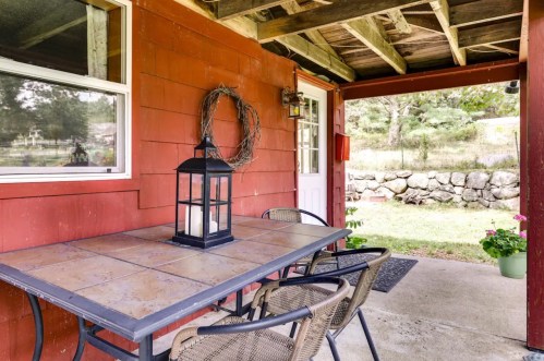 A cozy outdoor patio with a table, chairs, and a lantern, surrounded by greenery and a stone wall.