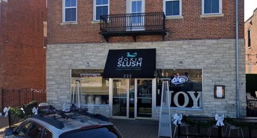 Exterior of Doxie Slush, a brick building with an open sign, featuring a balcony and festive decorations.