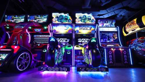 Colorful arcade games with neon lights, featuring motorcycle racing and driving simulators in a vibrant gaming space.