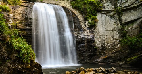 A serene waterfall cascading over rocky cliffs, surrounded by lush greenery and a tranquil pool below.