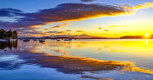 A serene sunset over a calm lake, with boats anchored and vibrant colors reflecting on the water's surface.