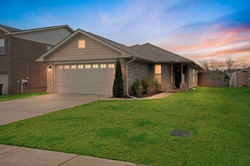 A single-story brick house with a garage, well-maintained lawn, and a colorful sunset in the background.