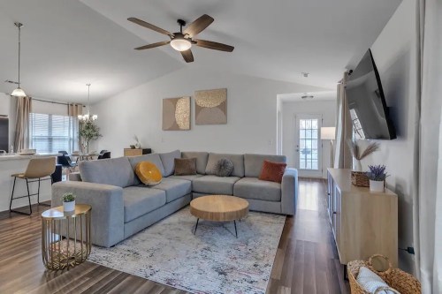Cozy living room with a gray sectional sofa, wooden coffee table, and modern decor, featuring a ceiling fan and TV.