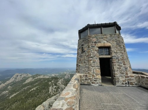 A stone lookout tower with a panoramic view of mountains and valleys under a cloudy sky.