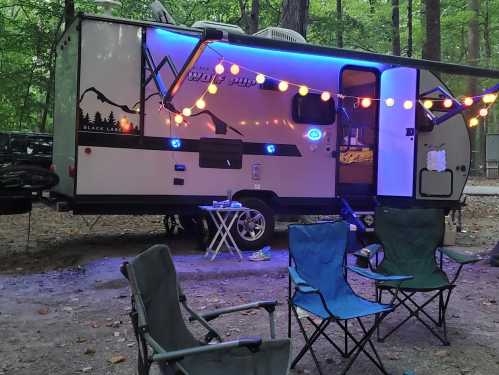 A cozy camper with colorful lights, surrounded by chairs in a wooded campsite.