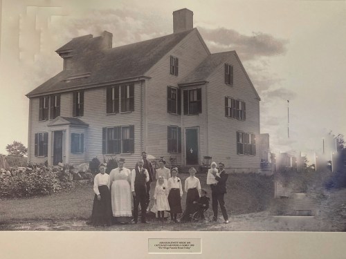 A historic black-and-white photo of a large family in front of a two-story house, with children and adults posing together.