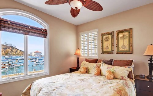 Cozy bedroom with a view of a harbor, featuring a bed, lamps, and decorative wall art.