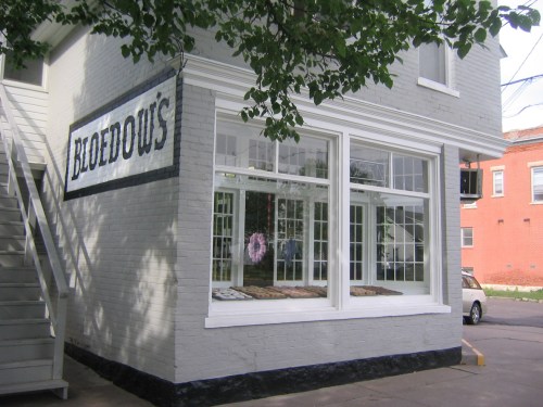 A corner building with a sign reading "Bloedows," featuring large windows and a decorative wreath.