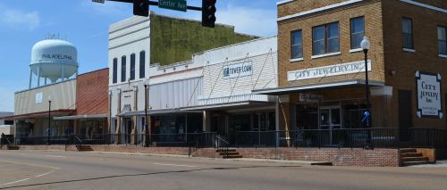A row of historic buildings in a small town, featuring shops and a water tower in the background.