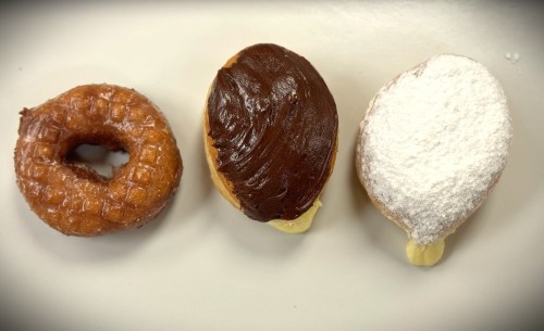 Three donuts: a glazed ring, a chocolate-covered filled donut, and a powdered sugar-covered filled donut.