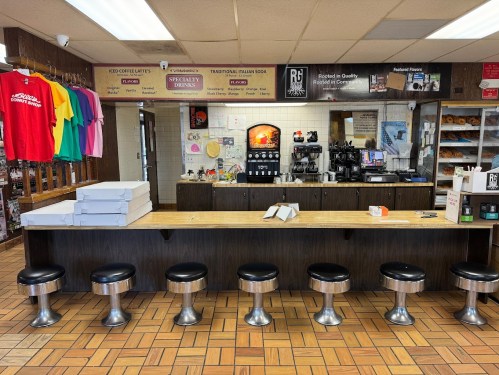 A cozy café interior featuring a counter with stools, coffee machines, and pizza boxes on the counter.