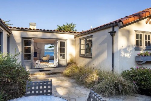A charming courtyard with a stone patio, leading to a cozy interior and a view of the ocean in the background.