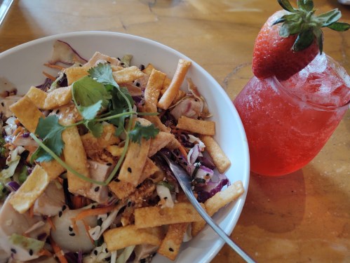 A colorful salad topped with crispy strips and cilantro, alongside a refreshing strawberry drink.