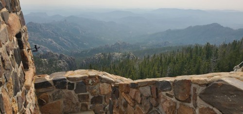 A scenic view from a stone structure overlooking misty mountains and dense forests in the distance.