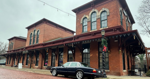 A classic car parked in front of a historic brick building on a cloudy day.