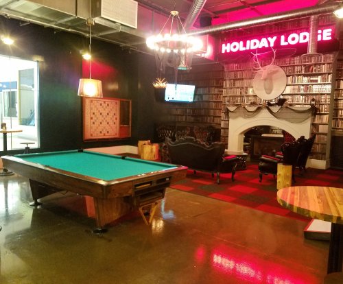 Cozy lounge area with a pool table, vintage seating, and a decorative fireplace under a "Holiday Lodge" sign.