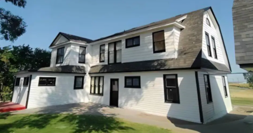 A two-story white house with black trim and multiple windows, set against a clear blue sky.