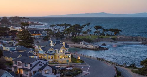 A coastal view at sunset featuring colorful houses, a winding road, and the ocean with distant hills.