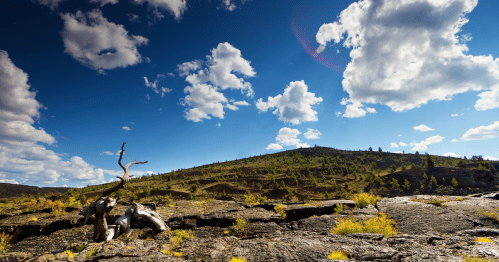 A scenic landscape featuring a rocky foreground, green hills, and a blue sky with fluffy clouds.
