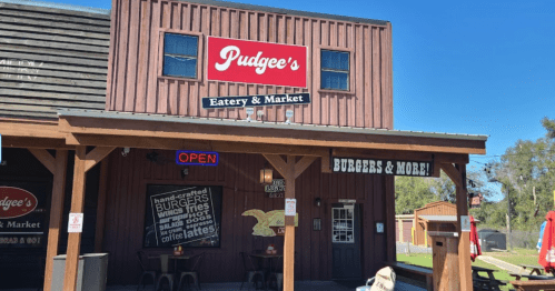 Exterior of Pudgee's Eatery & Market, featuring a wooden facade, "Open" sign, and outdoor seating area.