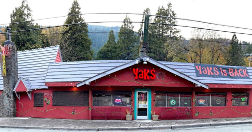 A colorful restaurant exterior with "Yak's is BACK" sign, surrounded by trees and mountains in the background.