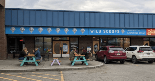 A colorful ice cream shop with outdoor seating, where people enjoy ice cream on a cloudy day.
