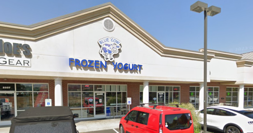Exterior of a frozen yogurt shop named "Blue Cow Frozen Yogurt," featuring a red van parked outside.