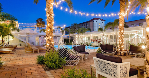 A beautifully lit pool area with palm trees, lounge chairs, and decorative string lights at dusk.