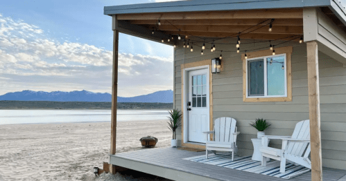 A cozy beach house with string lights, two chairs, and a scenic view of mountains and water in the background.