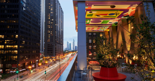 Cityscape view from a modern balcony, featuring colorful ceiling art and bustling street lights below.