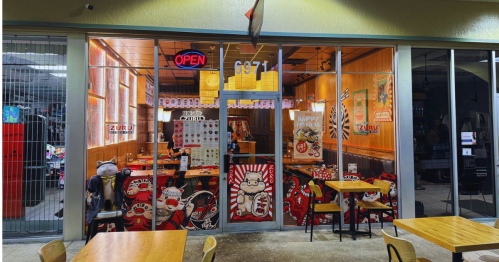 A vibrant restaurant entrance with an "Open" sign, colorful decor, and tables visible through large glass windows.