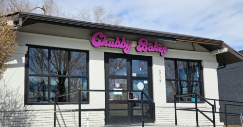 Exterior of the Chubby Baker bakery, featuring a sign and large windows, with a clear blue sky above.