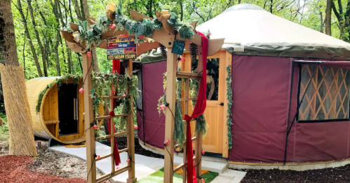 A cozy yurt surrounded by greenery, featuring a decorative entrance with flowers and ribbons.